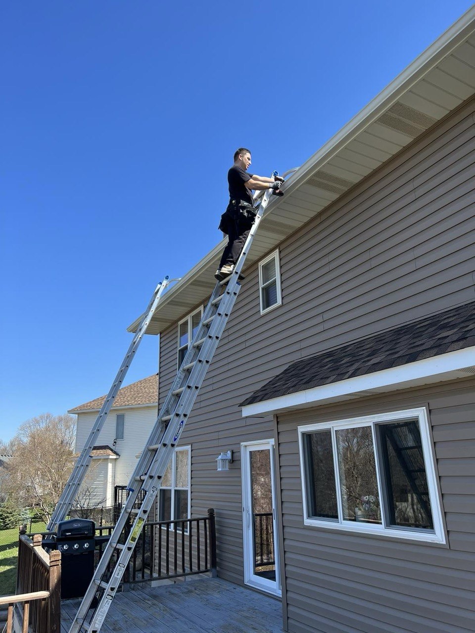 Vitalii working on a ladder installing gutters on a home